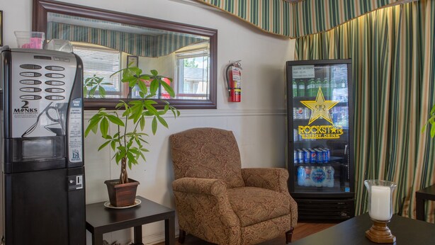 Une pièce équipée d’une machine à café, d’un distributeur automatique, d’une plante en pot, d’un fauteuil à motifs et d’une table avec une bougie.