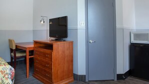 Une chambre d’hôtel avec un bureau en bois, une télévision, une porte et un four à micro-ondes.