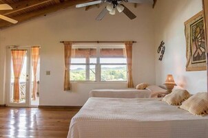 A room with two beds, a ceiling fan, a window with curtains, and a door leading outside.