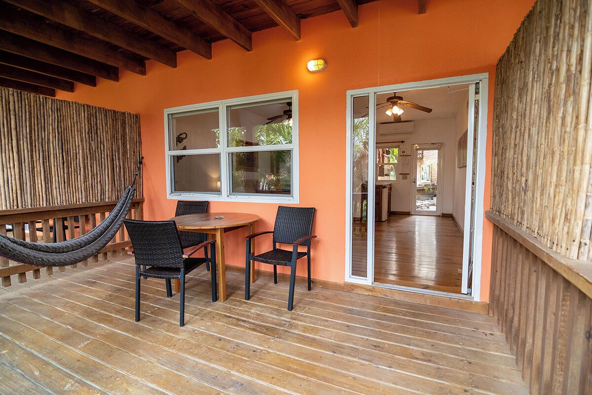 Eine Terrasse im Freien mit einem Holztisch und -stühlen, einer Hängematte und einer Glastür zu einem Innenraum.