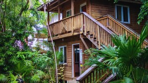 A wooden house with a balcony and stairs, surrounded by lush greenery. - Hotel Posada Las Orquideas (Roatan)
