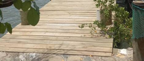 Un muelle de madera que lleva a una pequeña construcción de madera con techo de paja, con vista a una masa de agua y un fondo de bosque.