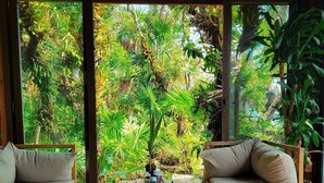 A room with a checkered floor, two sofas, a coffee table, and a view of lush greenery through large windows. - Hotel Posada Las Orquideas (Roatan)