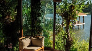 A room with a checkered floor, a sofa, a table, and a view of a body of water and greenery outside. - Hotel Posada Las Orquideas (Roatan)