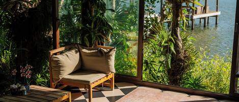 Una habitación con piso a cuadros, un sofá, una mesa y vistas al agua y vegetación.