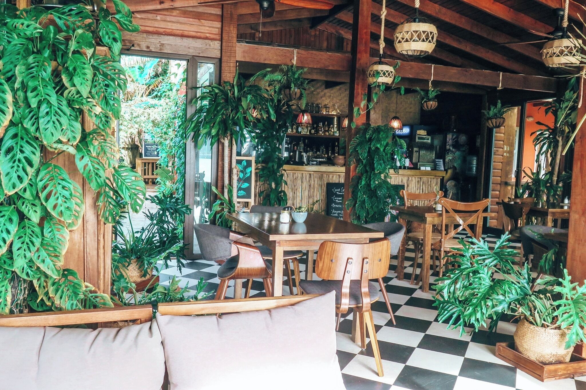 Un interior acogedor y rústico con muebles de madera, piso de cuadros y abundante vegetación.