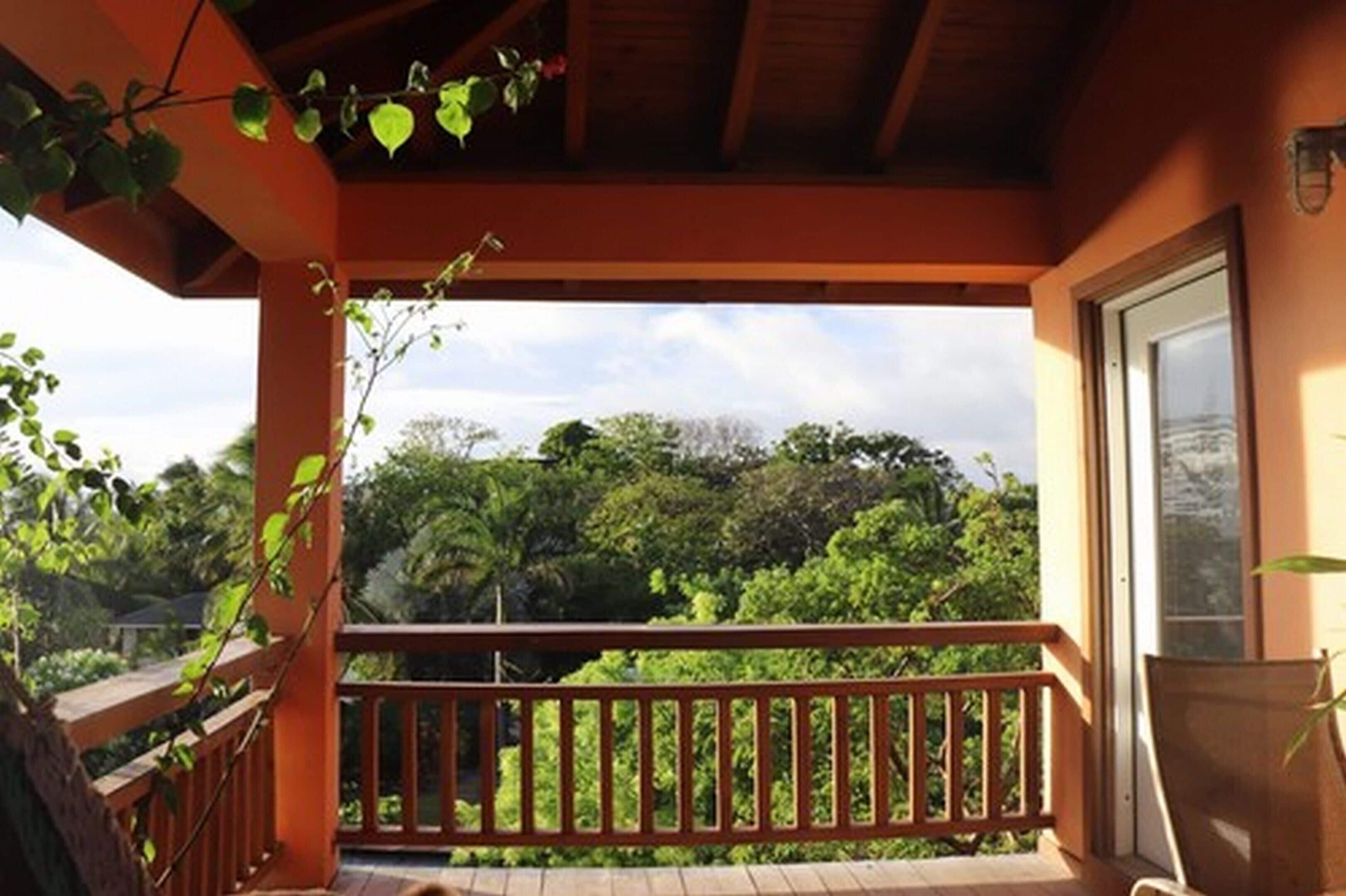 Un balcone con ringhiera in legno, una sedia e vista su vegetazione rigogliosa e alberi.