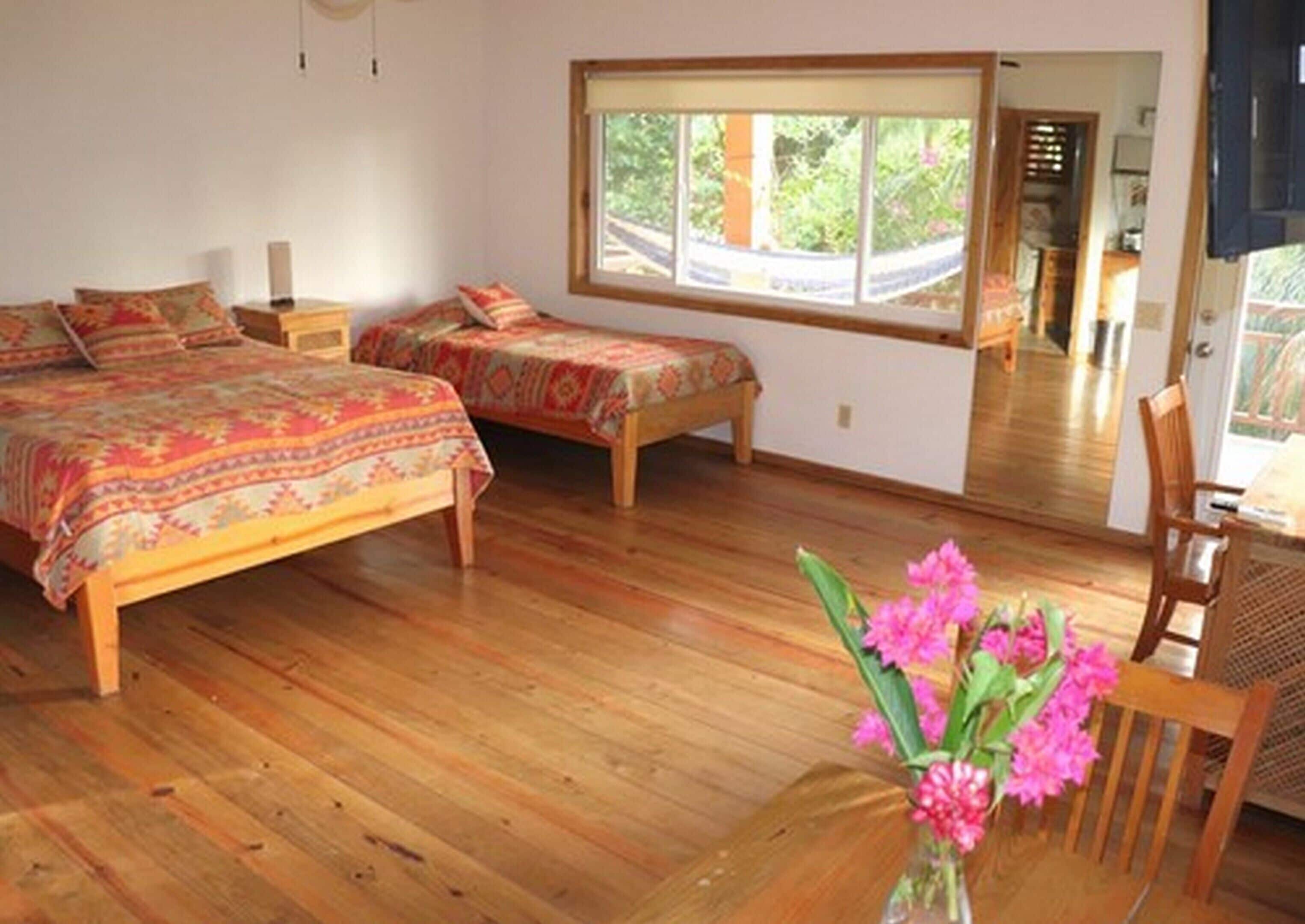 Ein Schlafzimmer mit zwei Betten, Holzboden, einem Fenster mit Blick und einem Spiegel, der den Raum widerspiegelt.
