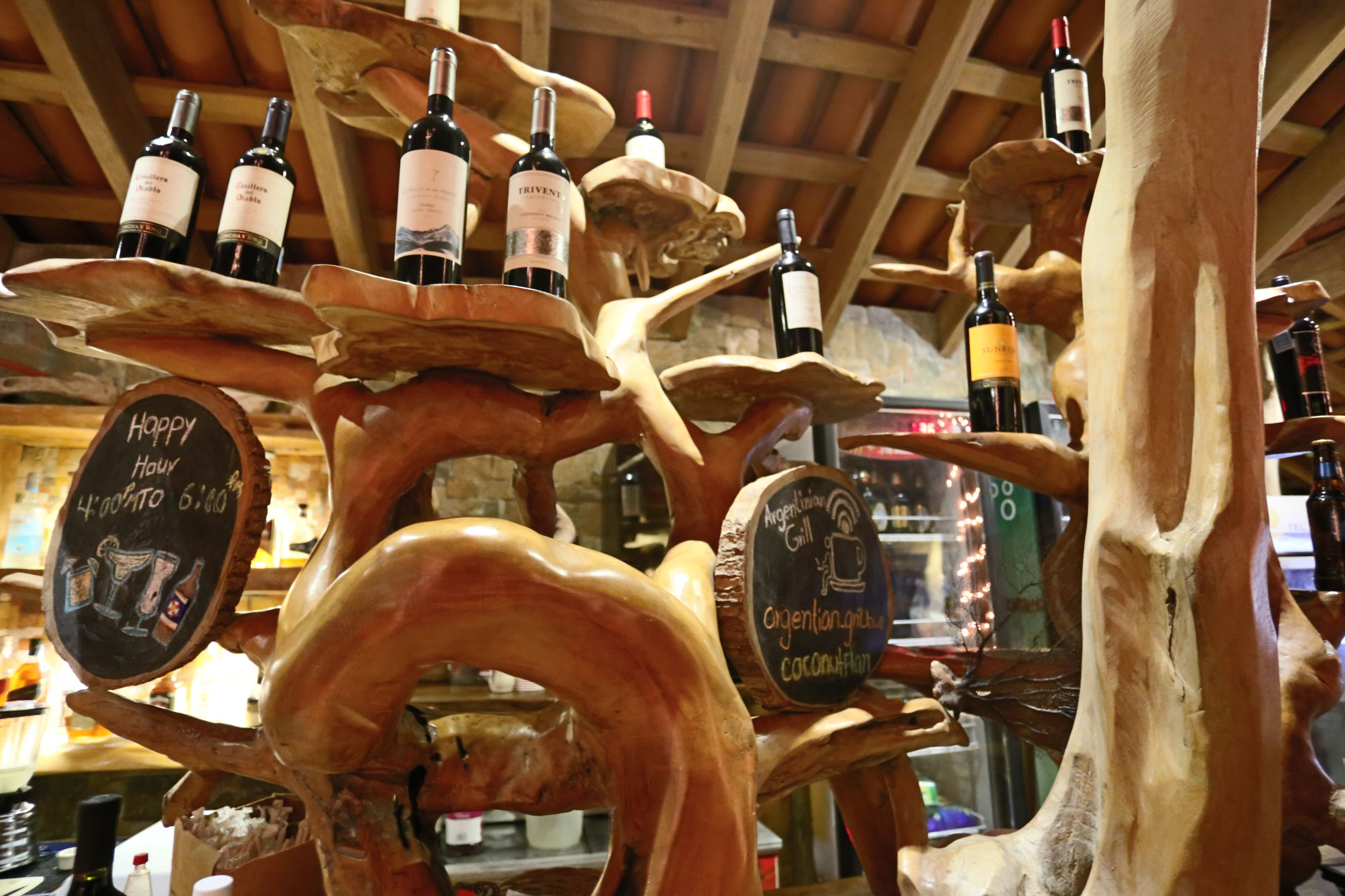 A wooden wine rack with bottles of wine and chalkboard signs with writing.