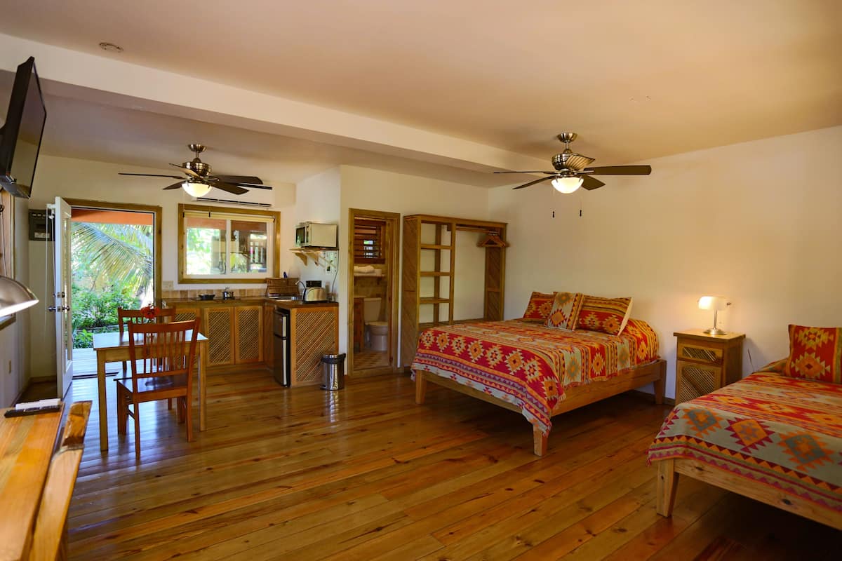 A bedroom with two beds, wooden flooring, ceiling fans, a TV, and a bathroom with a shower and toilet.