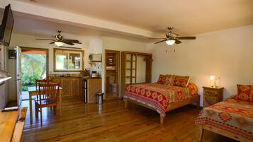 Un dormitorio con dos camas, piso de madera, ventiladores de techo, televisor y un baño con ducha e inodoro.