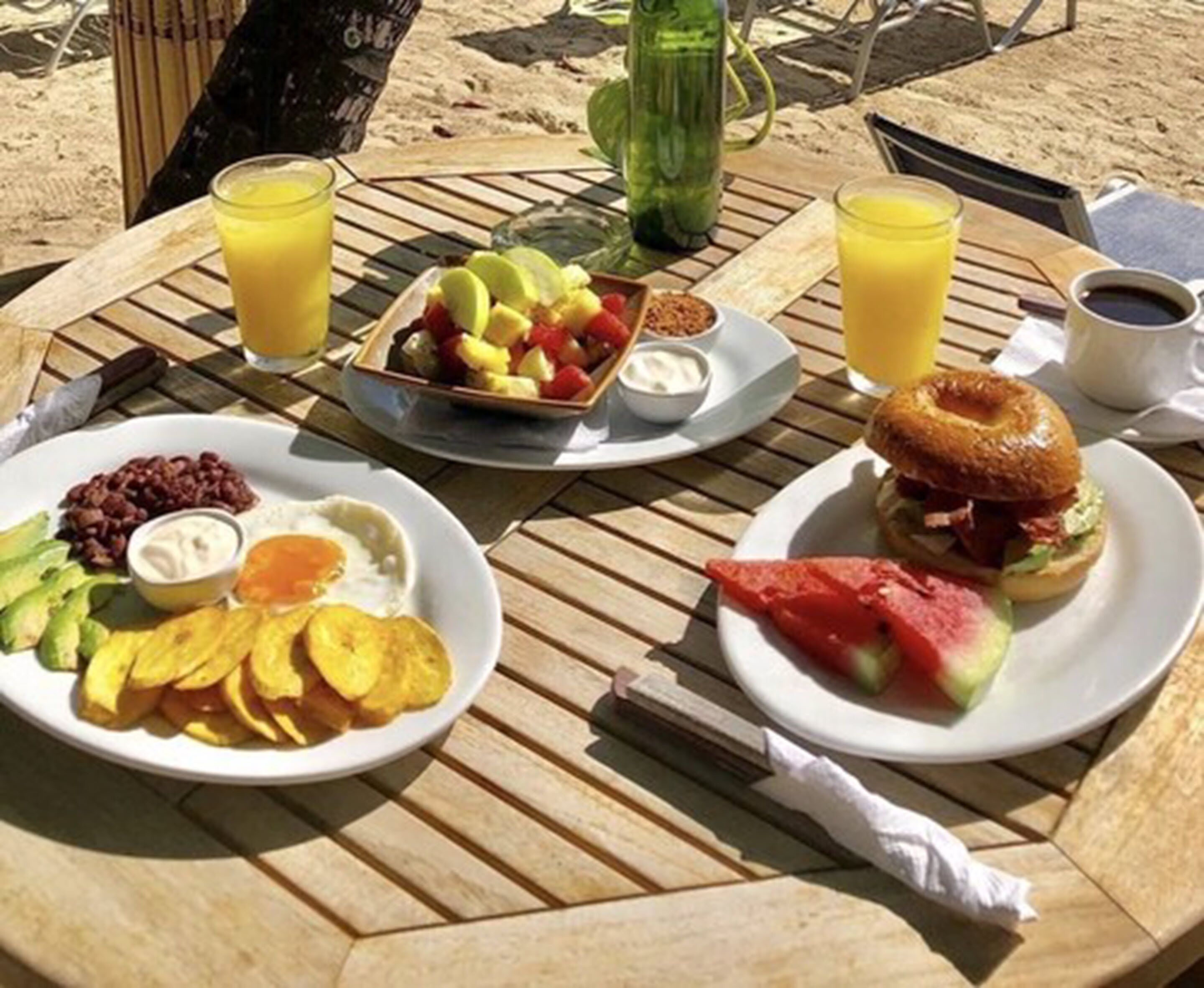 A table with breakfast items including eggs, avocado, chips, a fruit bowl, a sandwich, and drinks.