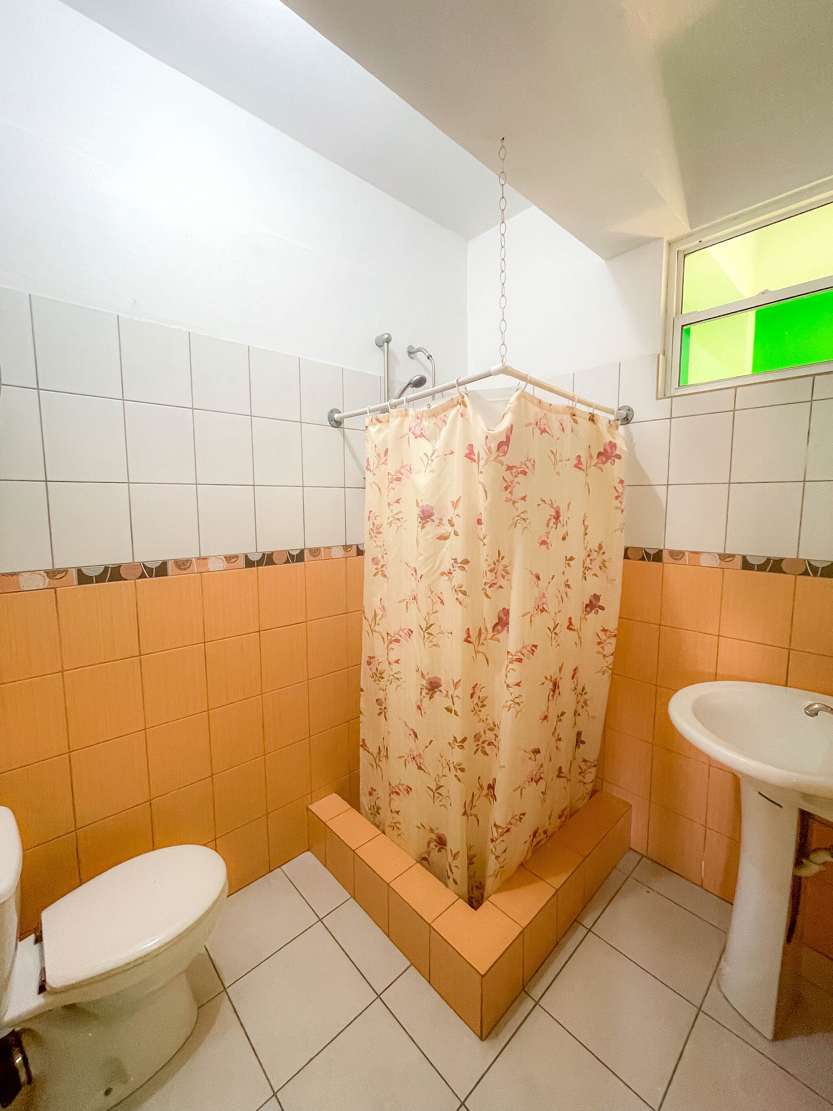 Une salle de bain équipée de toilettes, d’un lavabo et d’une douche avec un rideau de douche à motifs floraux.