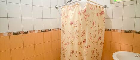 Une salle de bain équipée de toilettes, d’un lavabo et d’une douche avec un rideau de douche à motifs floraux.