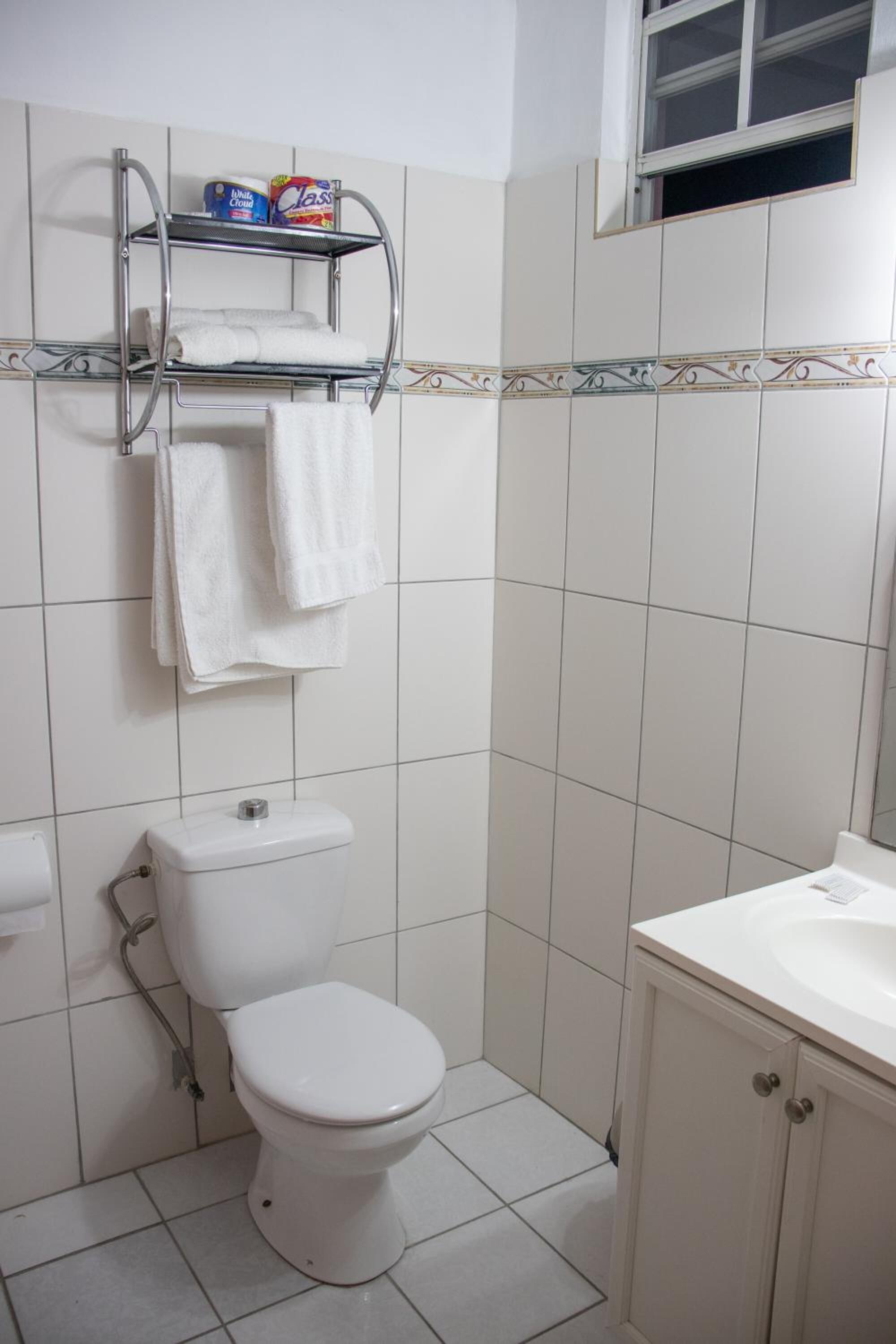 Casa de banho com sanita, lavatório e prateleira com toalhas e papel higiénico.