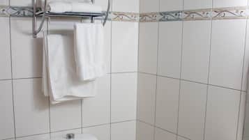 Casa de banho com sanita, lavatório e prateleira com toalhas e papel higiénico.