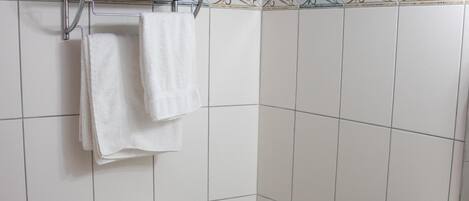 A bathroom with a toilet, a sink, and a shelf with towels and toilet paper.