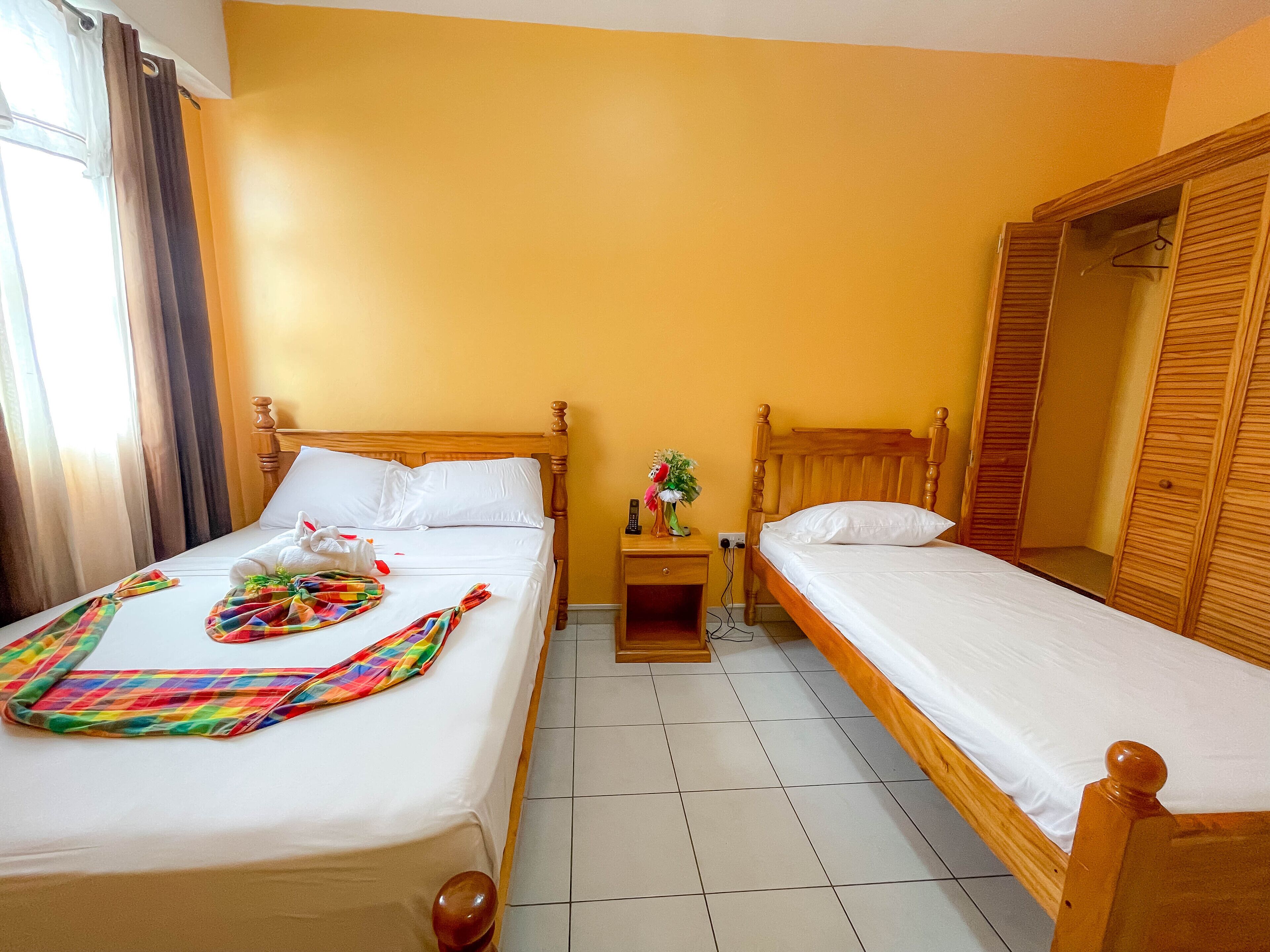 Una habitación de hotel con dos camas de madera, una mesita de noche con un florero y un armario de madera.