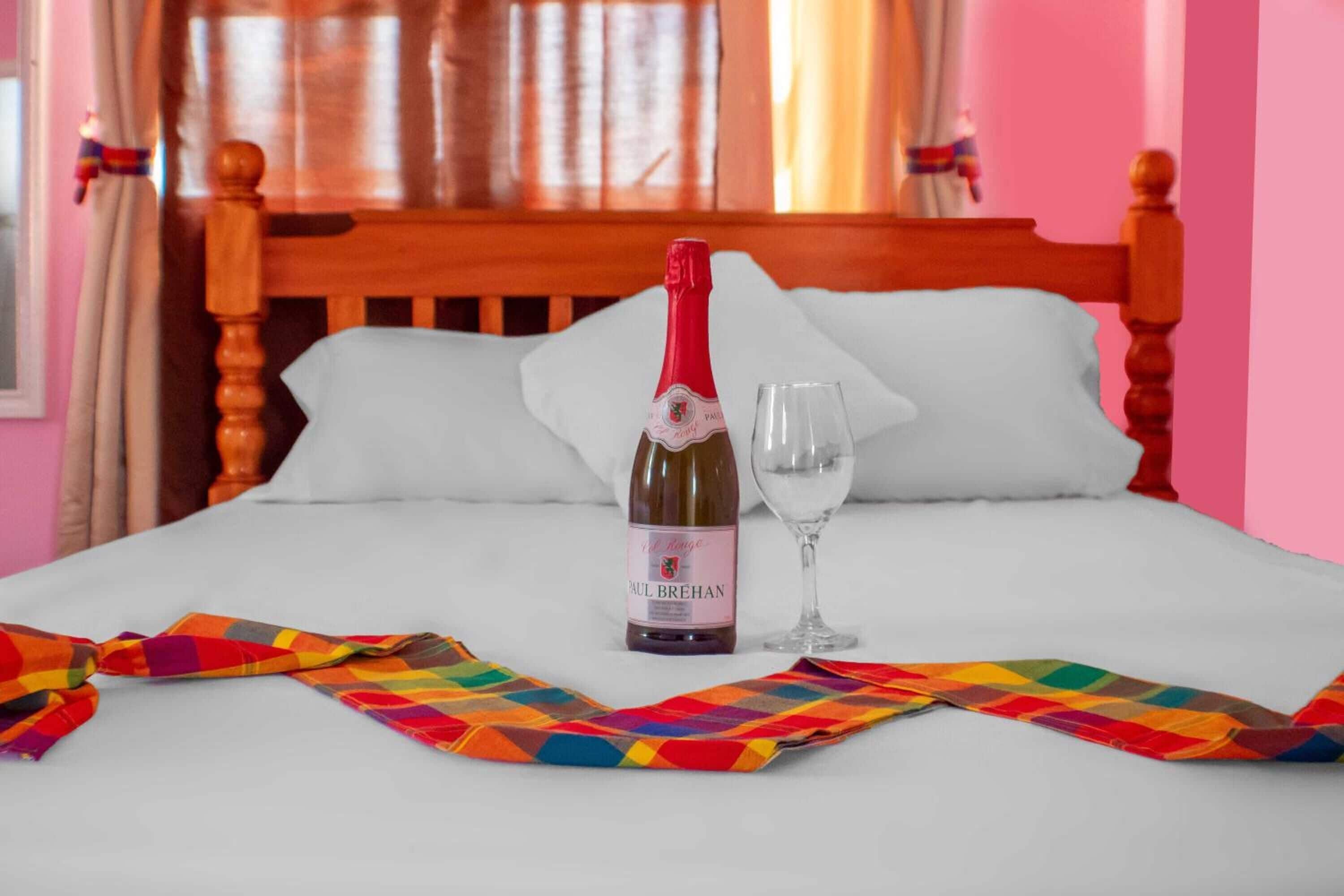A bed with a bottle of Paul Brehan wine and a glass, a colorful checkered cloth, and a wooden headboard.