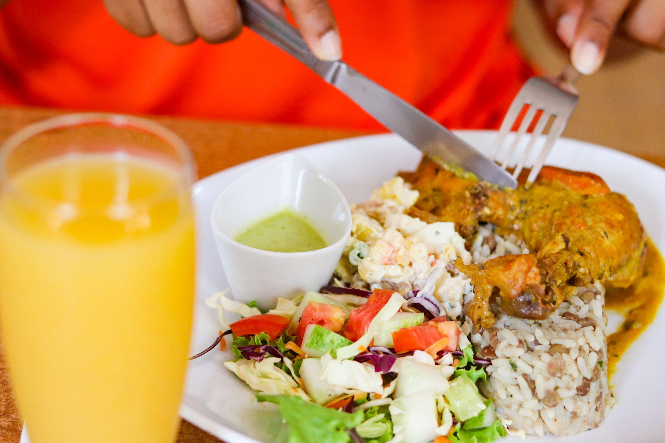 A plate with rice, a salad, and a piece of chicken, accompanied by a glass of orange juice and a small bowl of sauce.
