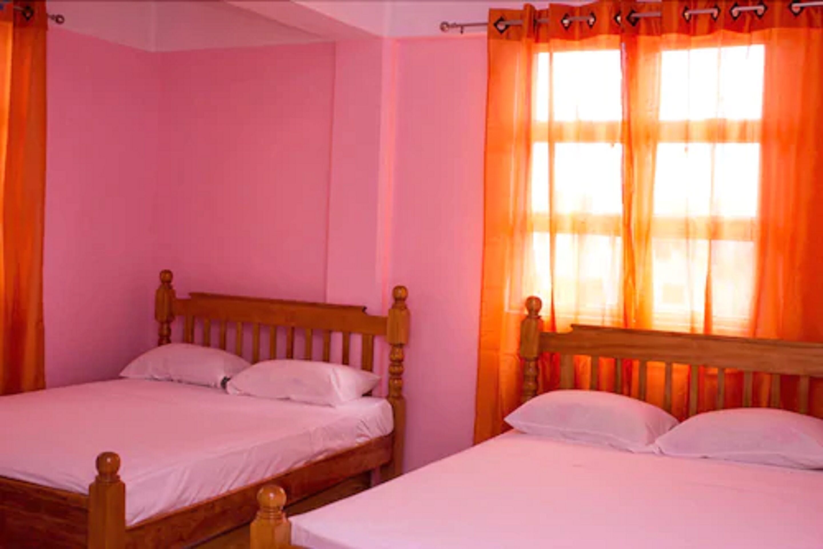 A room with two wooden beds, pink walls, and orange curtains.