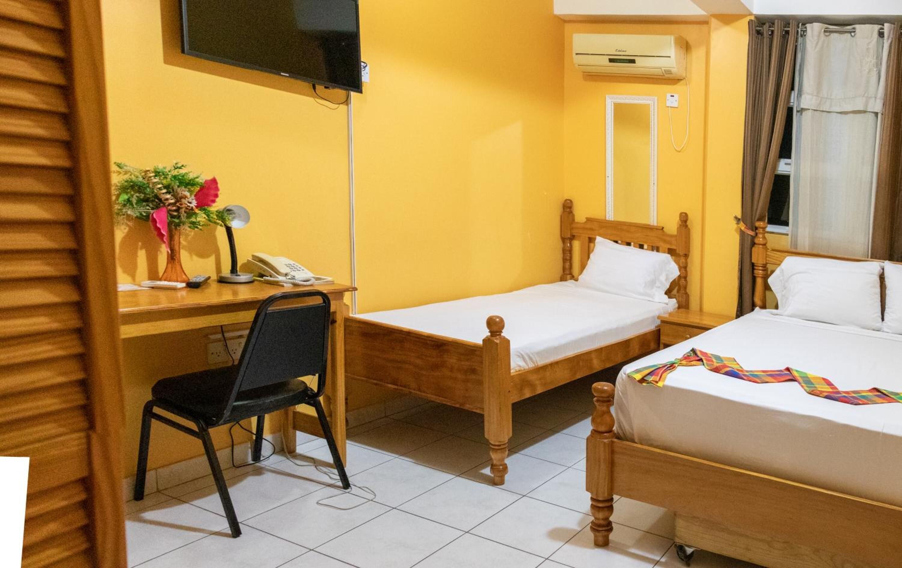 A hotel room with a wooden bed, a desk with a chair, a TV, and an air conditioning unit.