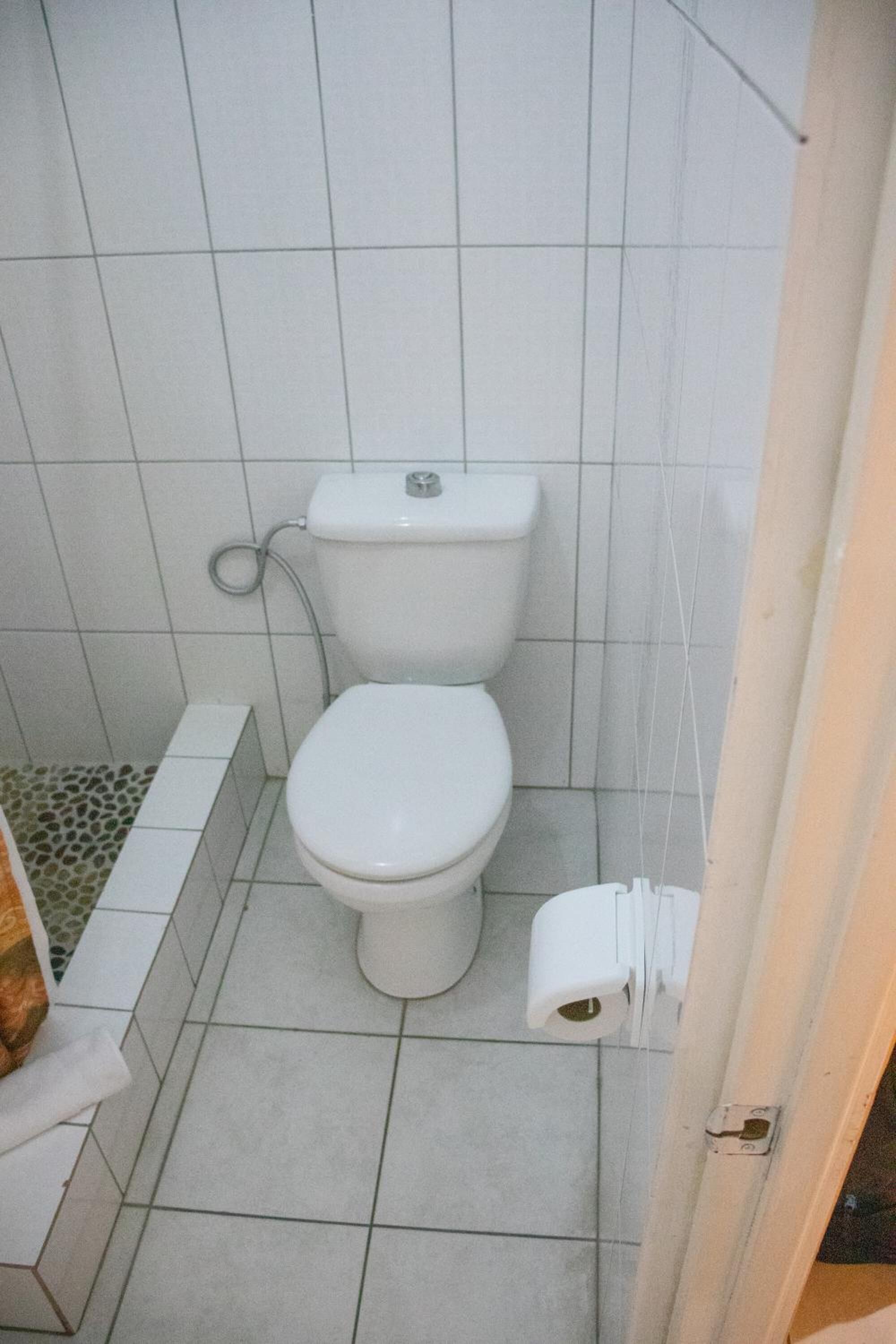 A small, tiled bathroom with a white toilet, a white sink, and a toilet paper holder.