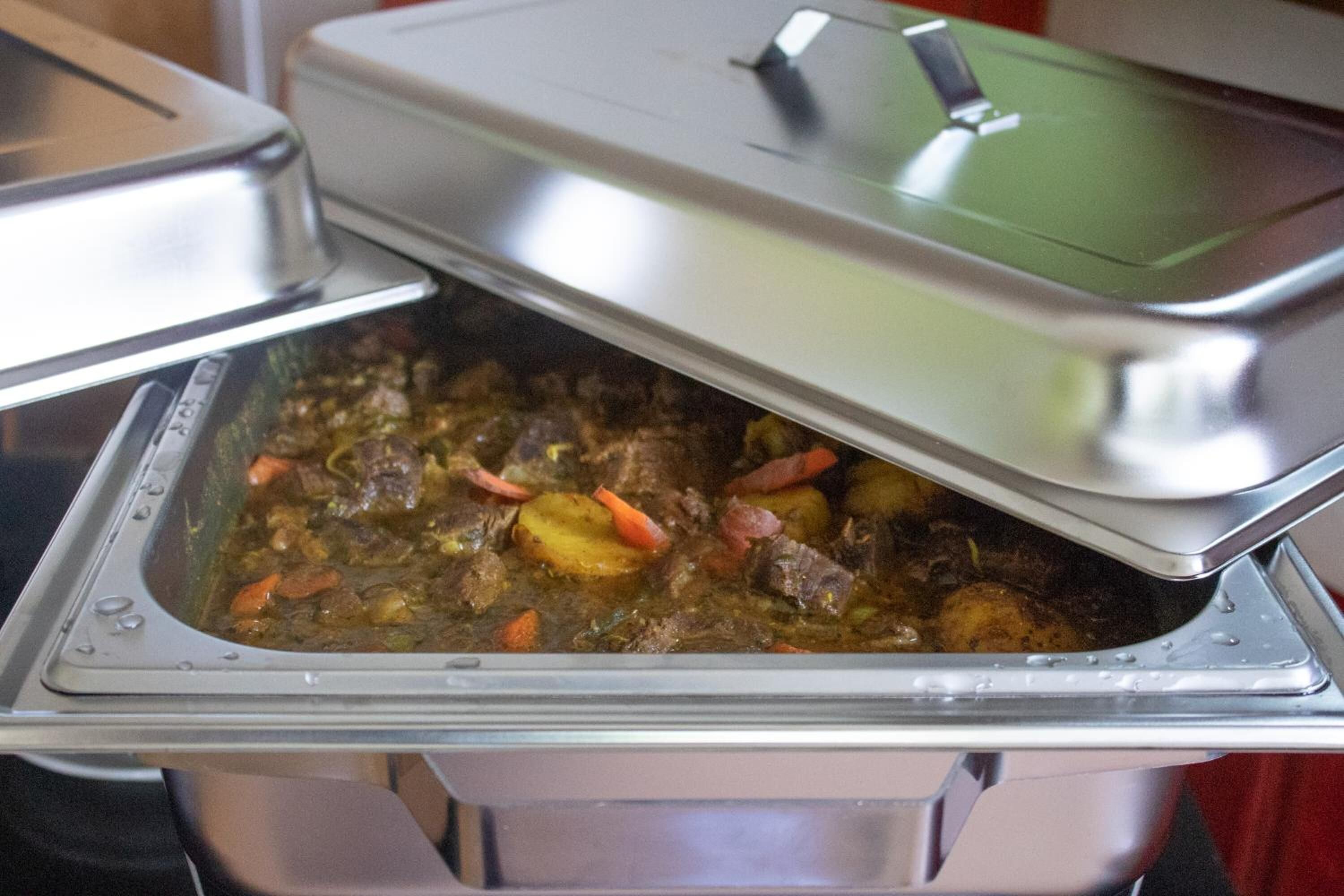 Een buffet met een afgedekte serveerschaal met een stoofpot van vlees en groenten.
