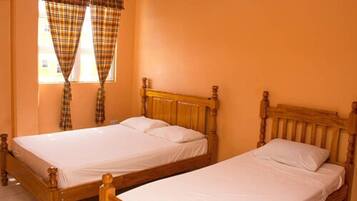 A room with two wooden beds, a window with plaid curtains, and a plain orange wall.