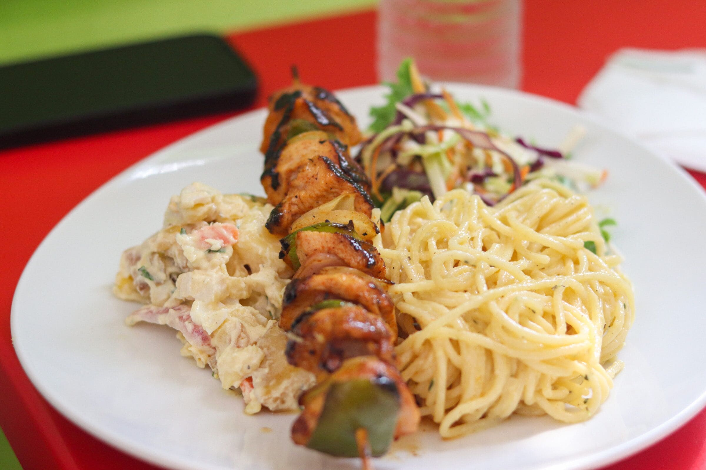 Een bord met gegrilde kipspiesjes, pasta en een salade.