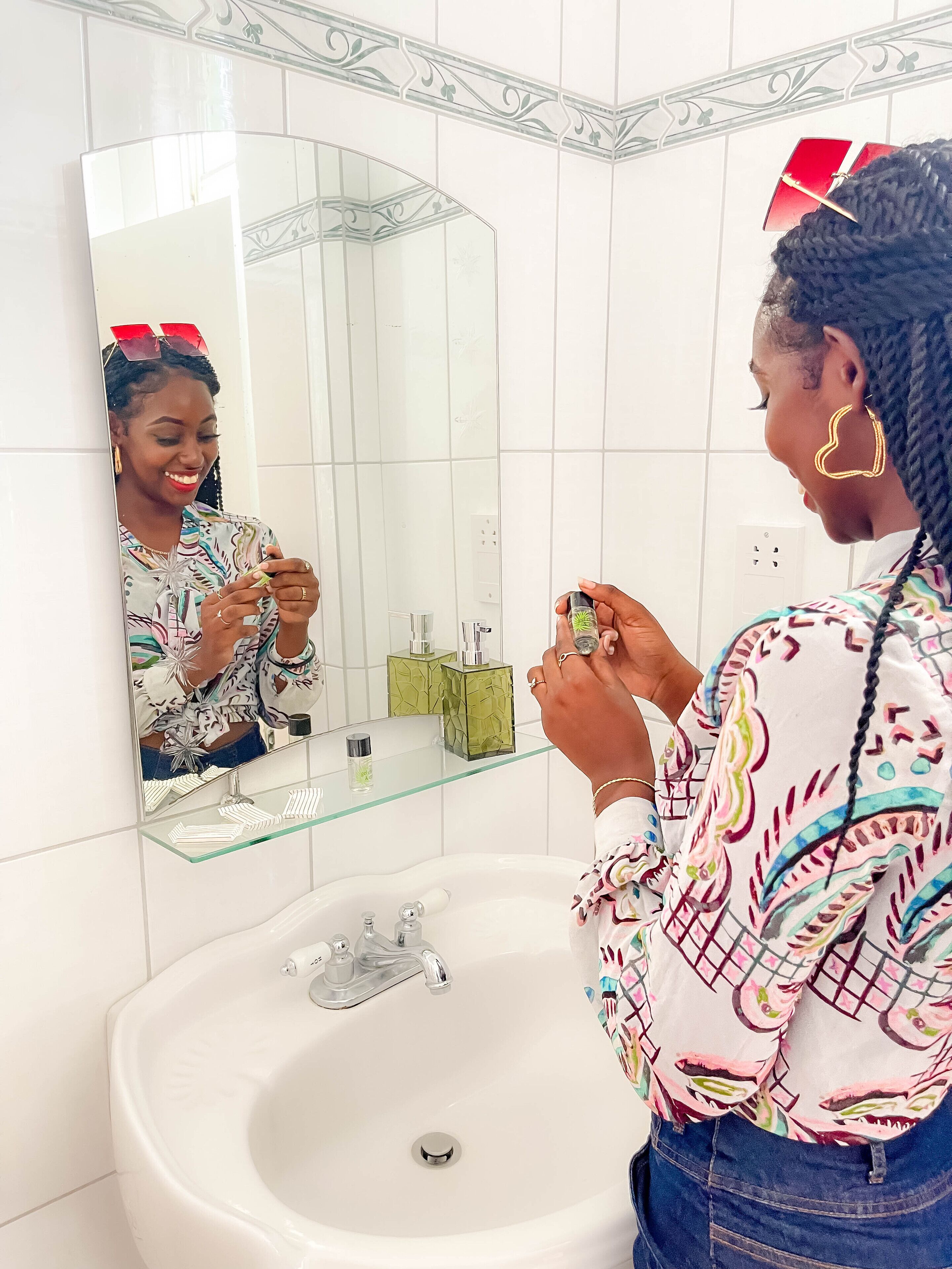 A bathroom with a white sink, a mirror, and a glass shelf with toiletries.