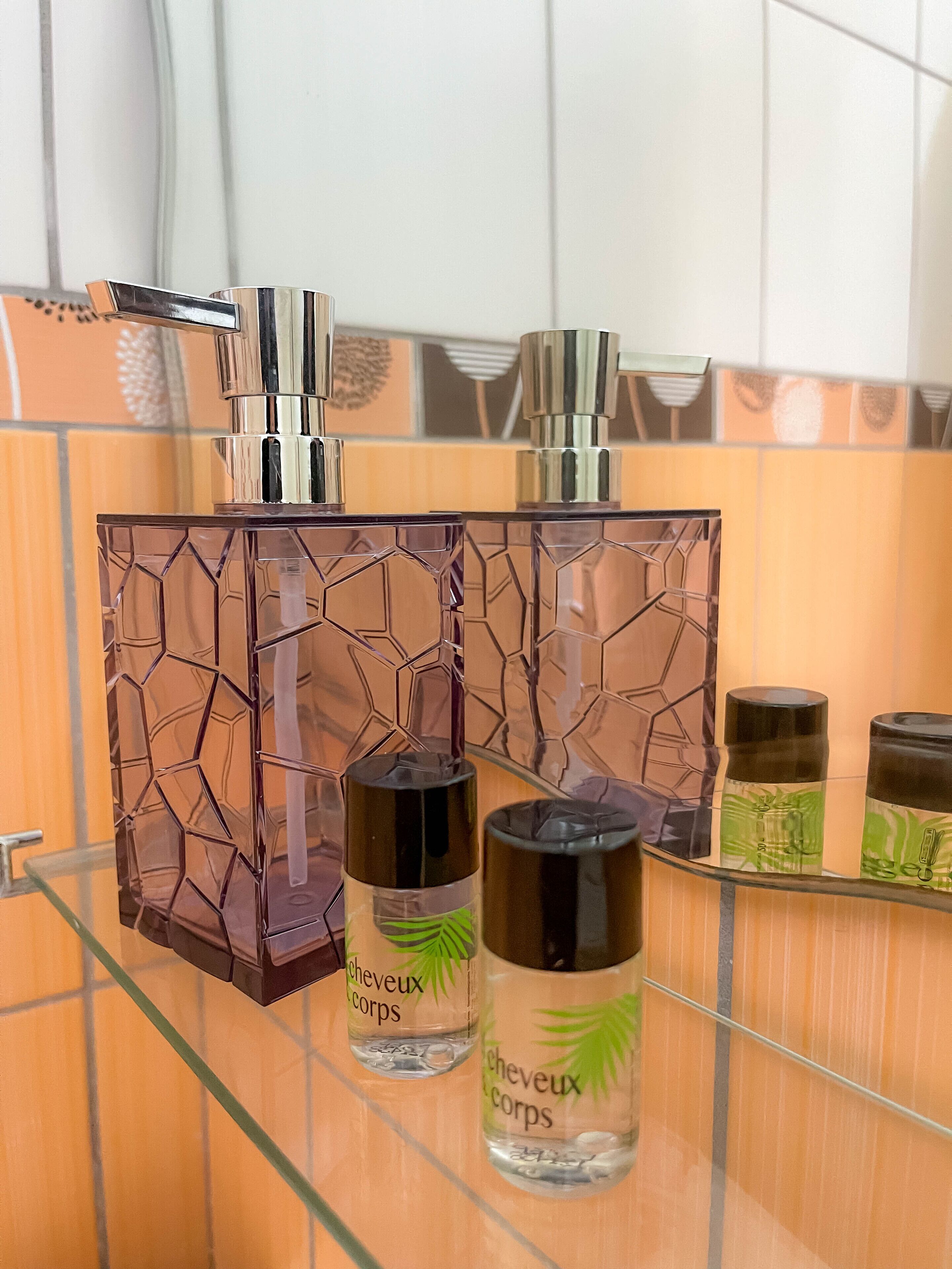 Ein Badezimmer mit einer Glasablage, auf der verschiedene Pflegeprodukte liegen, darunter eine große Flasche und zwei kleinere mit Etiketten.