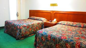 A hotel room with two beds, a wooden headboard, a bedside table with a lamp, and a green carpet.