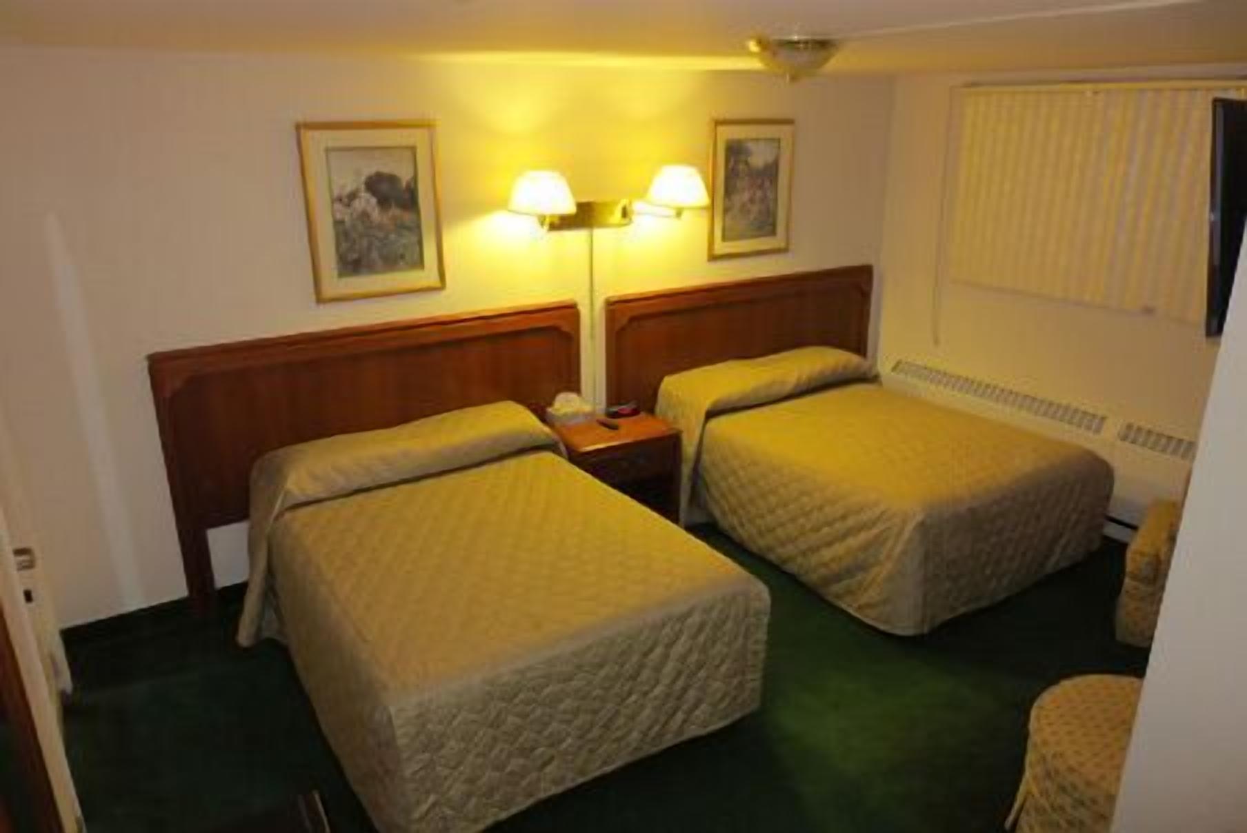 Habitación de hotel con dos camas, cabecero de madera, mesita de noche, dos lámparas fijadas a la pared y una ventana con persianas.