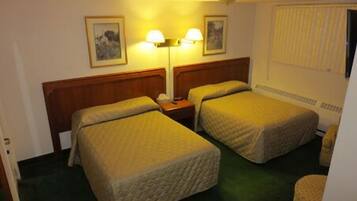 Habitación de hotel con dos camas, cabecero de madera, mesita de noche, dos lámparas fijadas a la pared y una ventana con persianas.