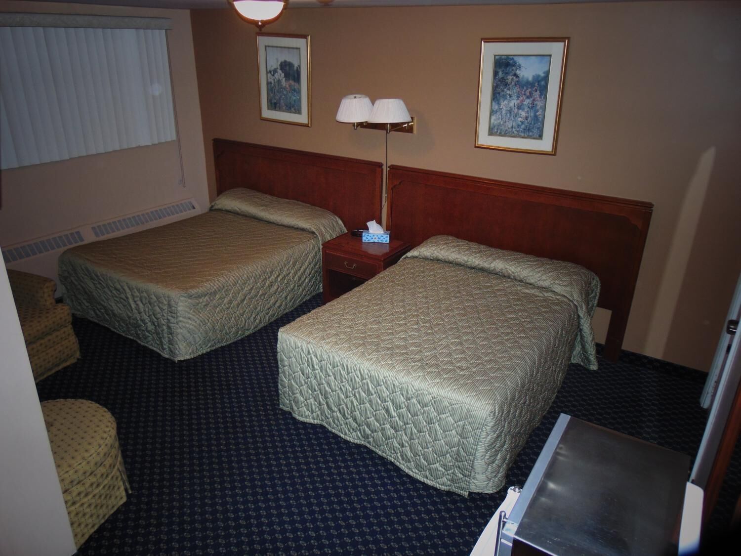 A hotel room with two beds, a nightstand, a lamp, and two framed pictures on the wall.