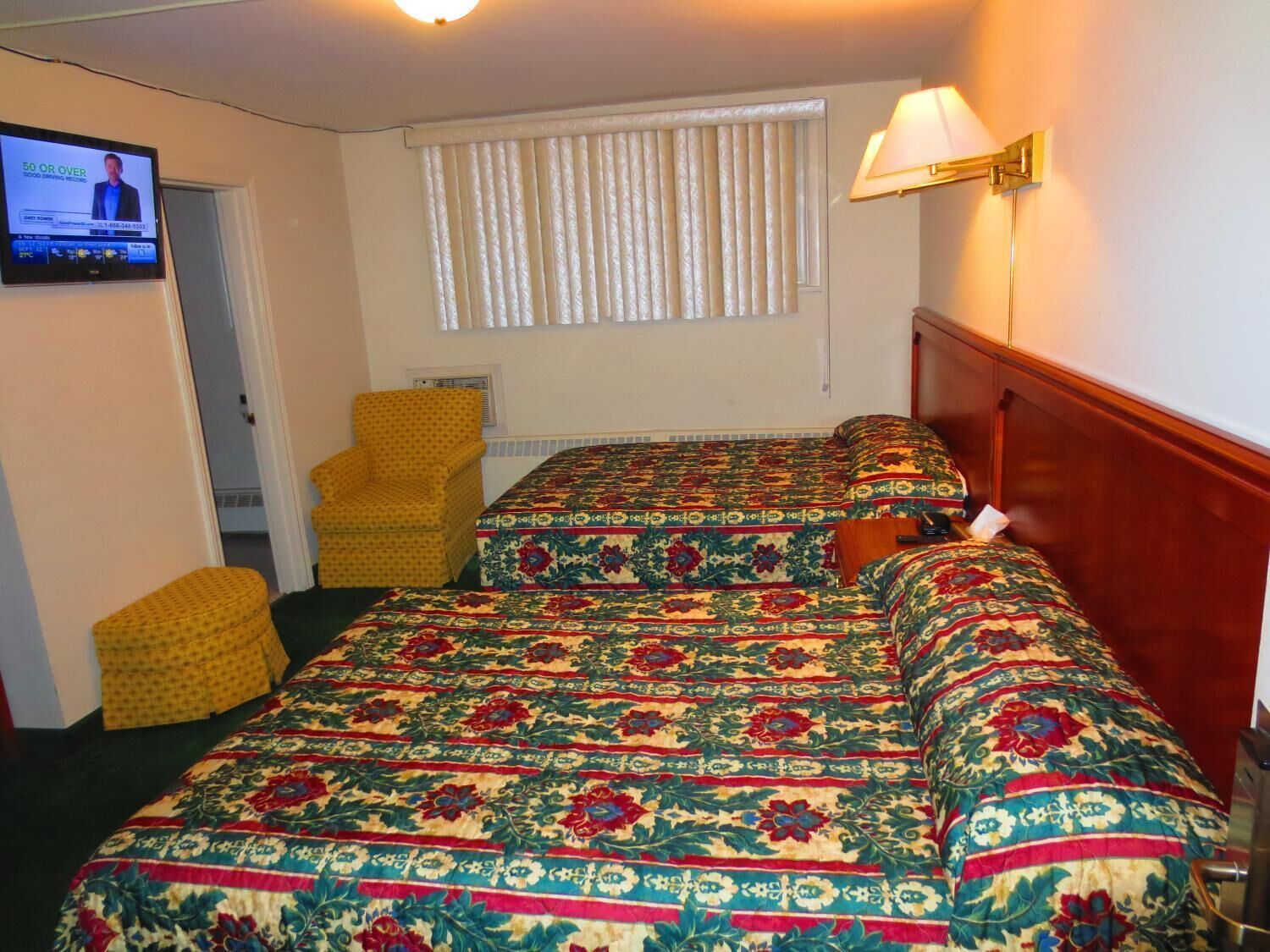 Una habitación de hotel con dos camas, un televisor, un sillón amarillo y una ventana con persianas.