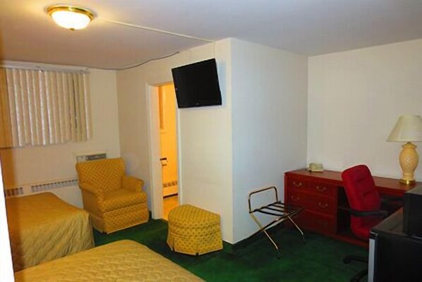 Una habitación con dos camas, un escritorio, una silla, un televisor y una lámpara.
