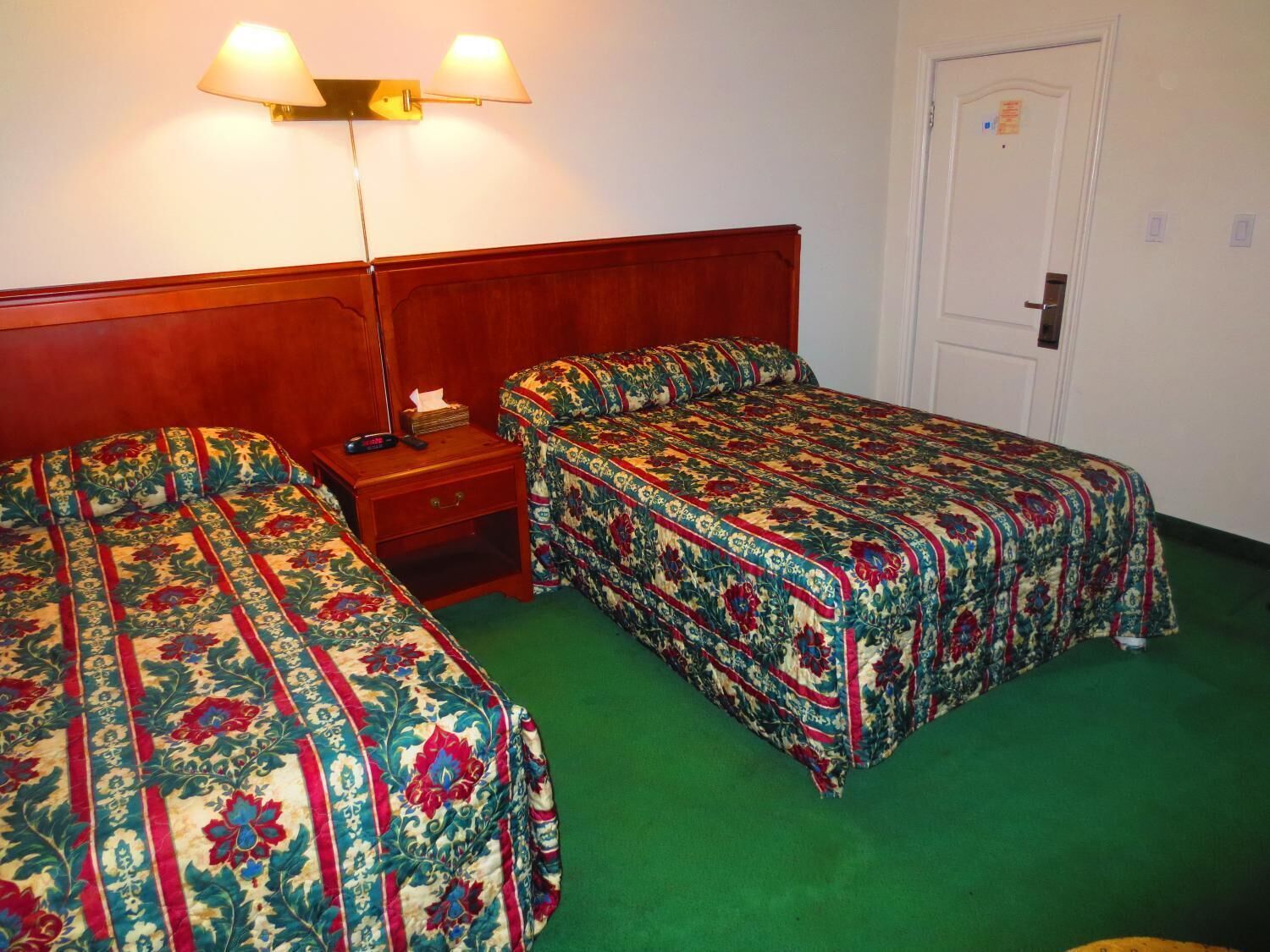 A room with two single beds, a nightstand, a lamp, and a door.
