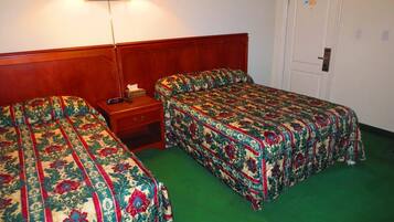 A room with two single beds, a nightstand, a lamp, and a door.