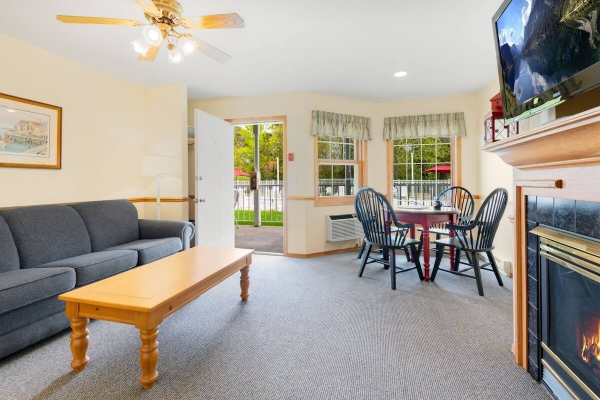 A cozy living room with a sofa, a wooden table, a fireplace, and a dining area with chairs and a table.