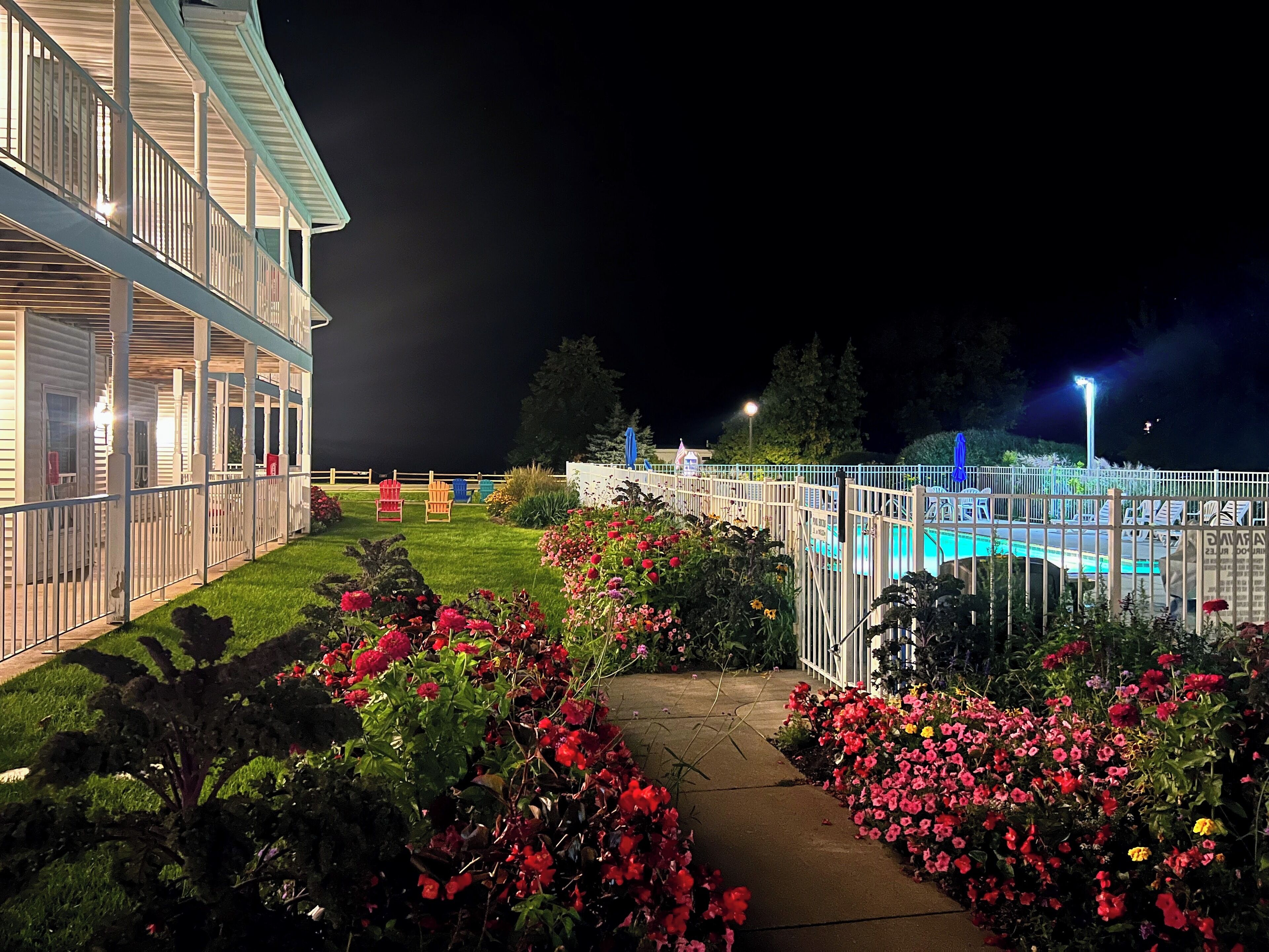 A hotel with a swimming pool, a covered outdoor area, and a well-maintained garden with flowers.