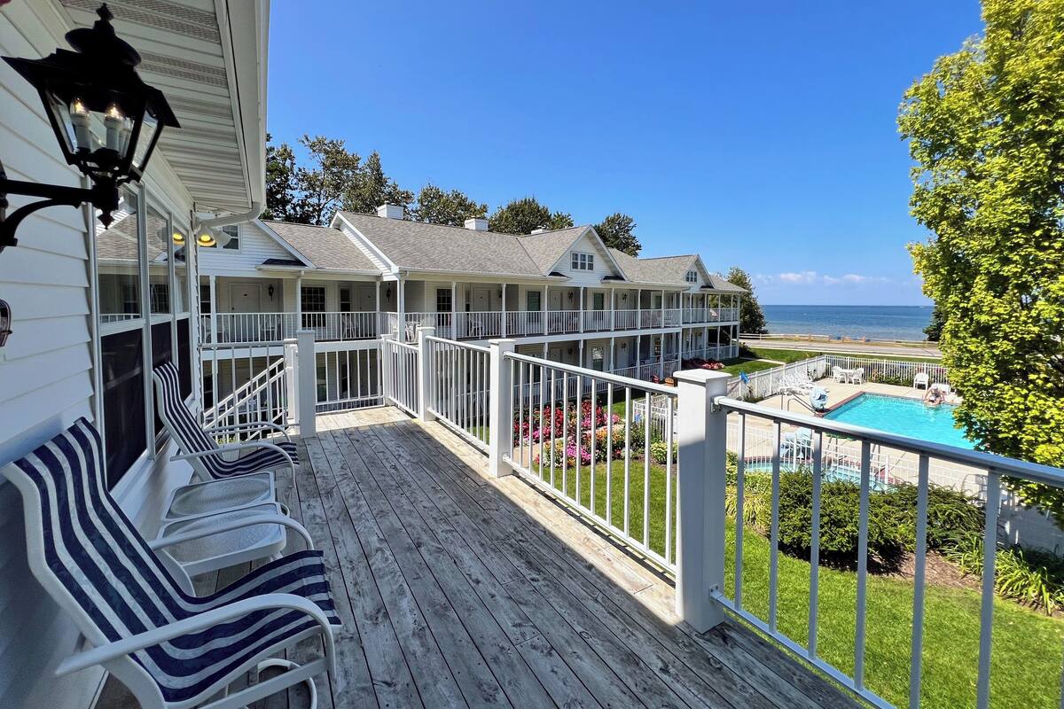 A multi-level wooden deck with white railings, outdoor seating, and a view of the ocean.