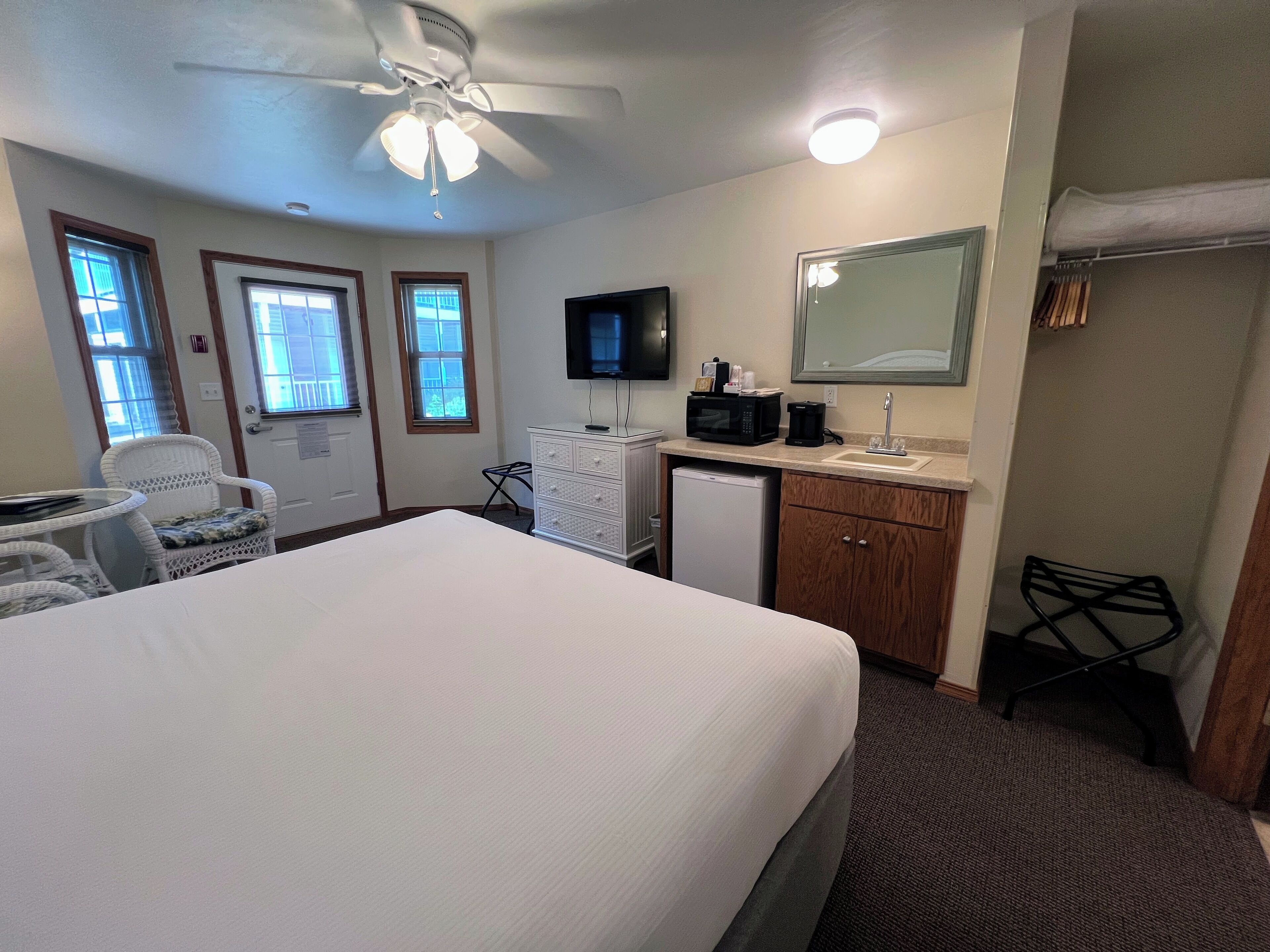 A hotel room with a bed, a desk, a chair, a microwave, a coffee maker, a sink, and a ceiling fan.