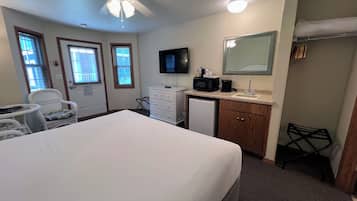 Habitación de hotel con cama, escritorio, silla, microondas, cafetera, lavabo y ventilador de techo.