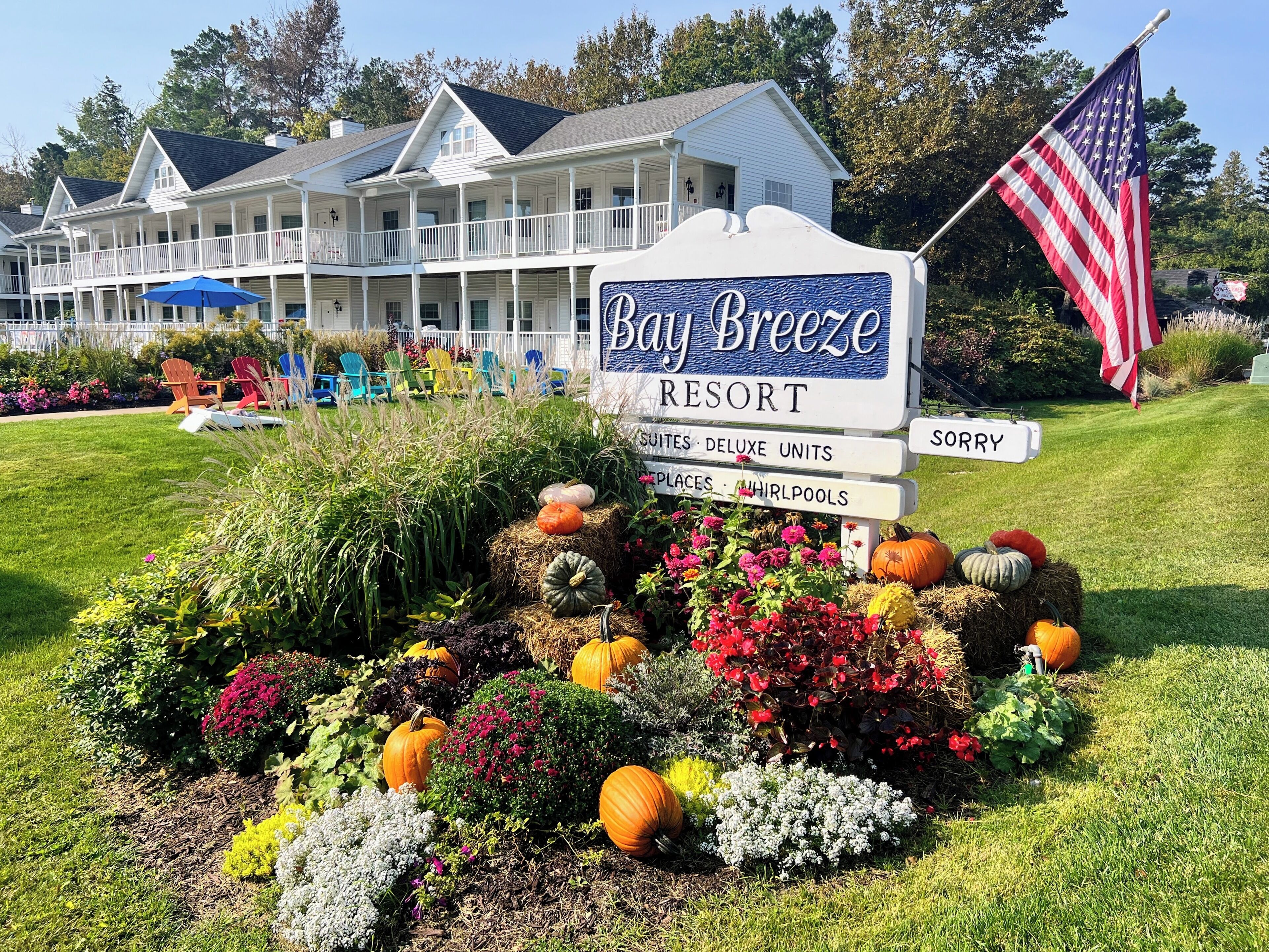 A sign for Bay Breeze Resort with a garden display of pumpkins and flowers.