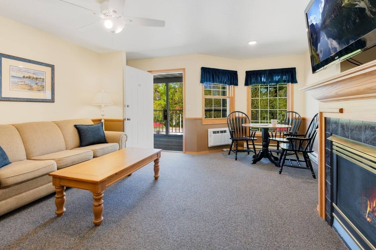 A living room with a sofa, coffee table, and a fireplace. There is a dining area with a table and chairs.