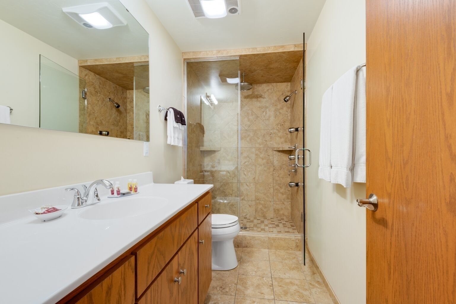A modern bathroom with a white sink, wooden vanity, a glass shower enclosure, and a toilet.