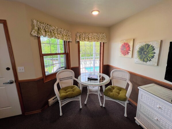 A corner room with two wicker chairs, a small glass table, and a white dresser. - Bay Breeze Resort (Ephraim)