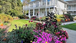 A two-story building with a covered porch and a well-maintained garden with various flowers and plants. - Bay Breeze Resort (Ephraim)